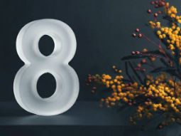 Стильное поздравление с 8 Марта: белая цифра восемь на темном фоне рядом с веткой мимозы